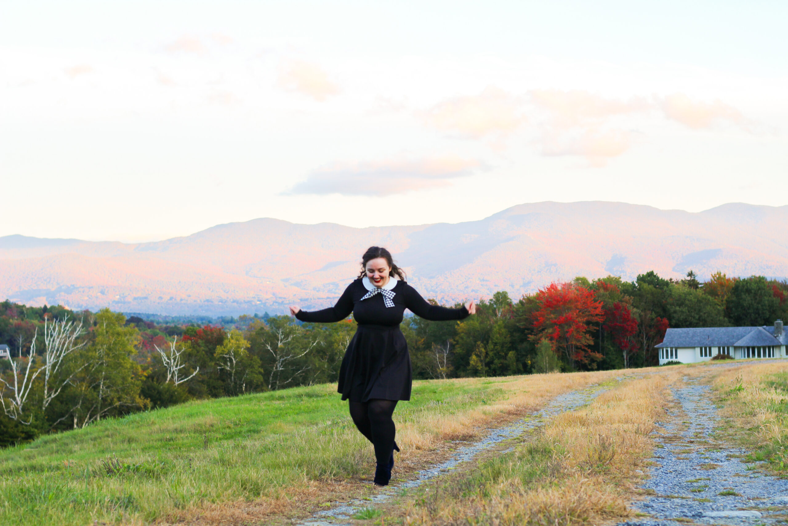 A photo of Joanna No Banana, who is the writer of this blog post, a white woman with brown, curly hair wearing a dark blue dress and black leggings running in a field with mountains in the background