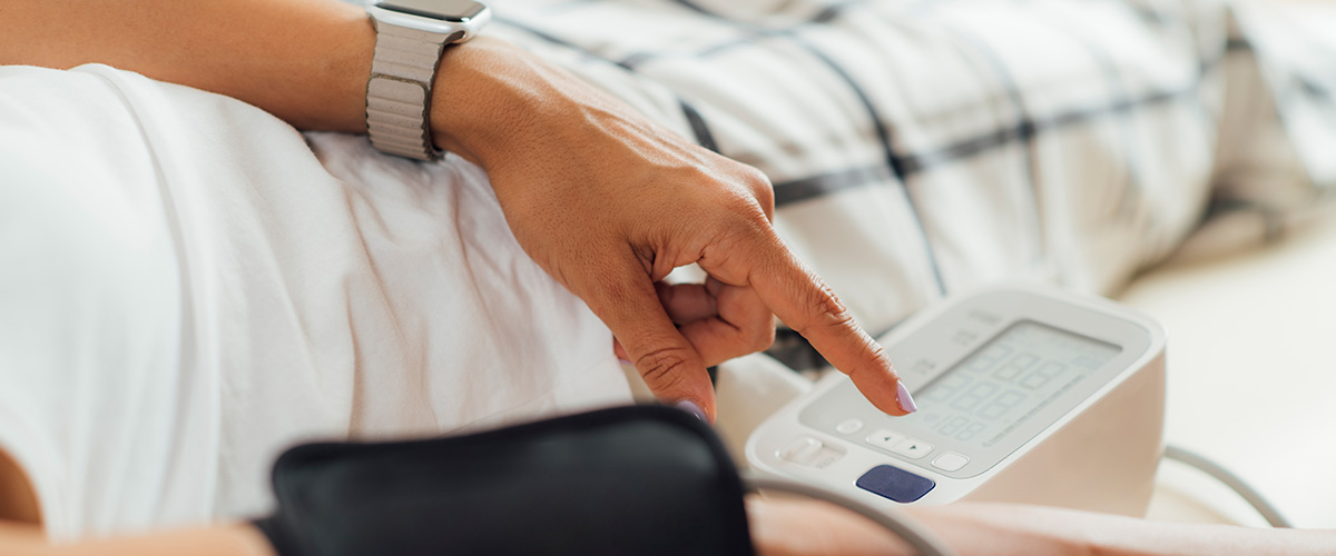 person laying on their back in bed wearing a blood pressure cuff checking their blood pressure with an at home testing device