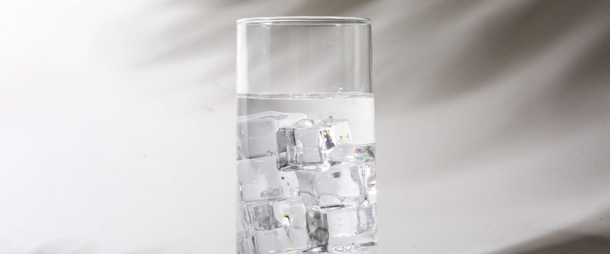 A glass of ice water in front of a shadowed white background