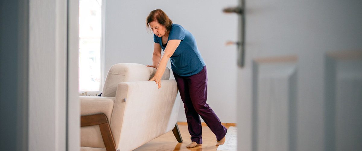 an older women in a blue shirt and dark pants holding onto the back of a couch
